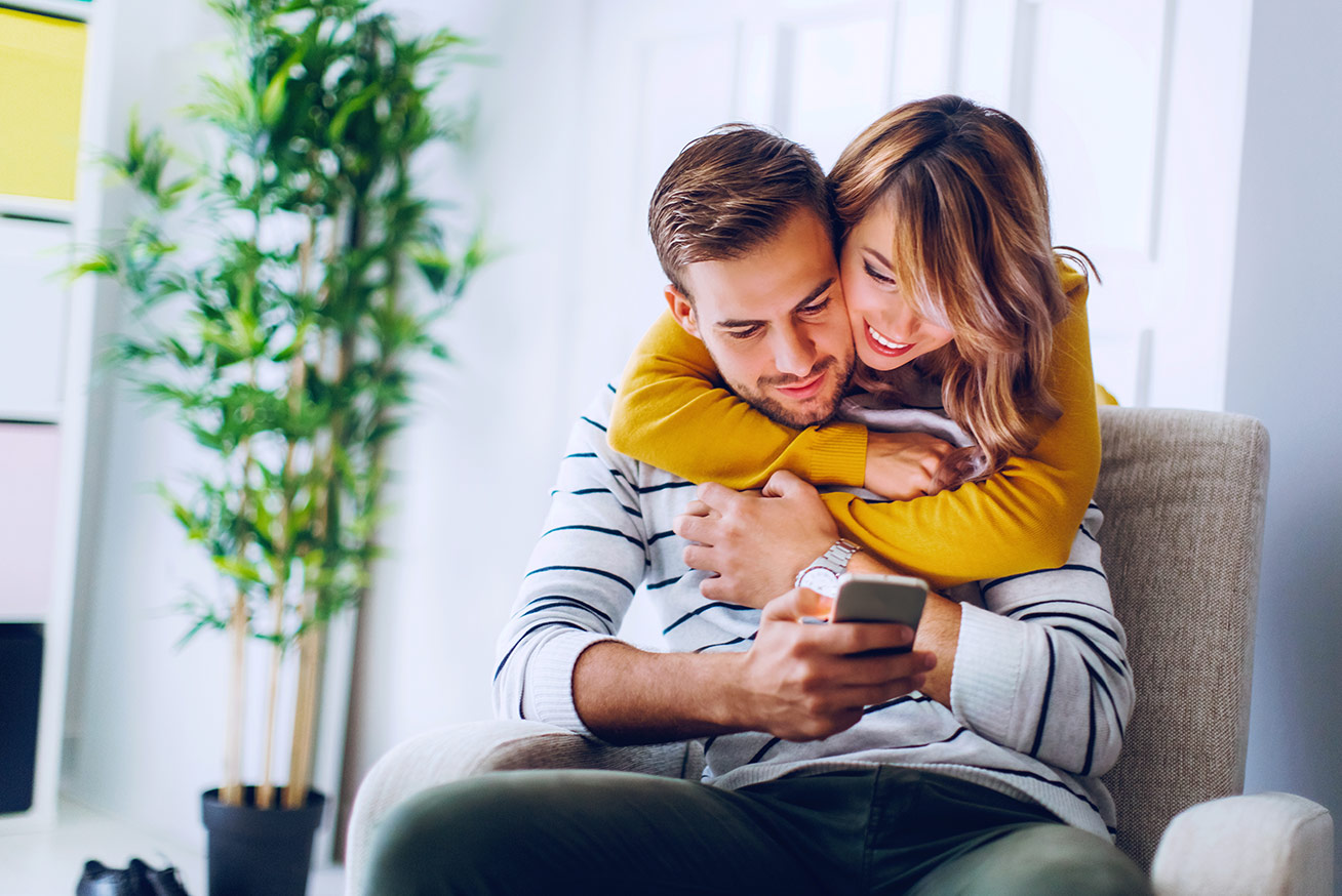 Happy Couple On Sofa looking at handheld